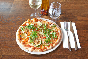 Silverware on Brown wooden table and White plate with round pizza and mushroom.