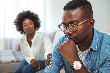 Upset couple at home. Handsome man and beautiful young woman are having quarrel. Sitting on sofa...