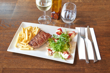 Wooden table and plate with Beef steack, french fries and tomato on salad.