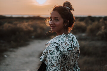Shallow focus of a stylish young female with her hair in a messy bun in a field during the sunset