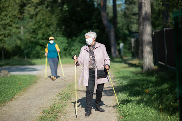 Senior women wearing medical masks walking with nordic walking poles during covid-19 pandemic