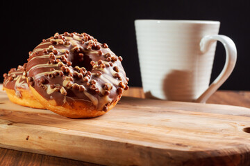 Fresh tasty chocolate with sugar icing donuts on a wooden board white tea cup in fore ground. Black background. Bakery product