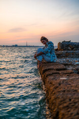 Vertical shot of a young female relaxing on stones surrounded by the sea during a beautiful sunset