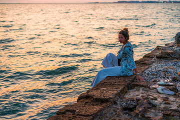 Young female with her hair in a messy bun sitting on rocks surrounded by the sea under the sunlight
