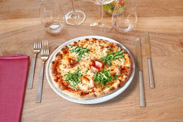 Silverware on Brown wooden table and White plate with round pizza and shrimp.