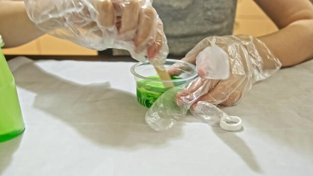A boy making green slime at home, DIY project, chemistry experiment, he pours the ingredients into a container and mixes them