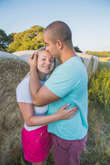 husband hugs and kisses his wife in a field with hay