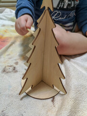 Baby decorates a wooden Christmas tree on a round stand
