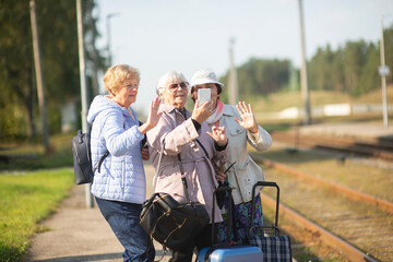 Group of smiling senior women take a self-portrait on a platform waiting for a train to travel...