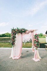 Elegant wedding arch made of pink flowers of hydrangea, roses and greenery on a spacious green lawn.
