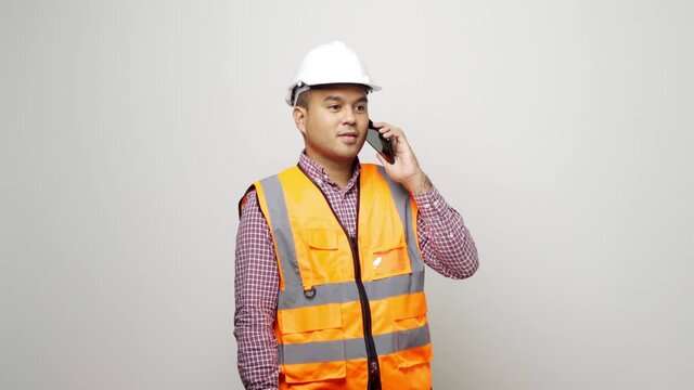 Asian mechanic talking with customer on phone to home service. Worker wearing hard hat using smartphone standing on isolated white background. 4k resolution.