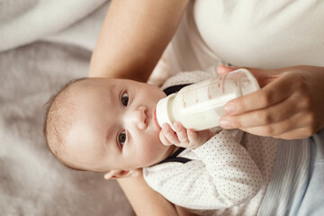 baby eats milk from a bottle and looks at camera