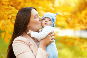 portraits of mom and baby in autumn park, mom hugs and kisses baby