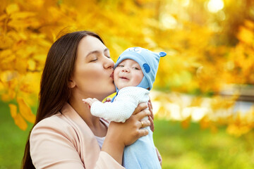 portraits of mom and baby in autumn park, mom hugs and kisses baby