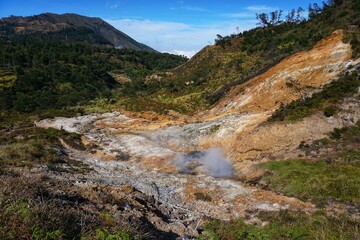 Sikidang crater tourist spot with a background of limestone mountain slopes under the blue sky.	