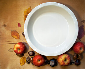 Empty ceramic cake tin and autumn leaves, apples and chestnuts on a wooden background. Autumn composition. Square orientation.