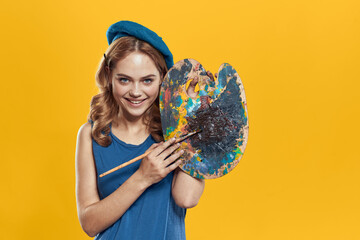 Fototapeta premium Woman with palette in blue hands takes paintbrush hobby artwork yellow background
