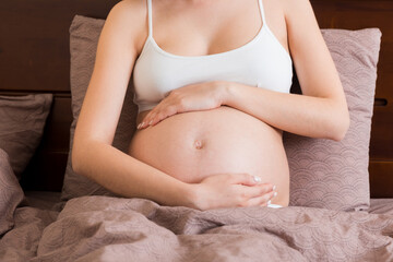 Fototapeta na wymiar Young pretty pregnant woman, in pain, sitting on bed in bedroom, preparing to give a birth