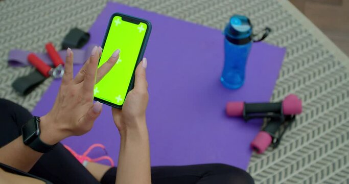 Fitness woman use smartphone with green screen after training at home. Healthy lifestyle. stretching, leaning forward. Training on distance.