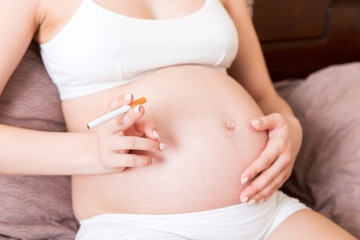 Pregnant woman smoking cigarette at home in bed