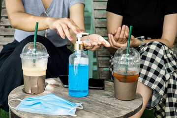 two female customers cleaning their hand  with alcohol gel at coffee shop, new normal concept