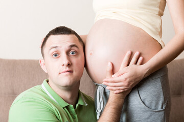 Young bearded man putting his ear close to his pregnant wifes abdomen and Listening it