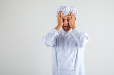 Male chef cook holding hands to head and smiling in hat and uniform and looking ashamed. front view.
