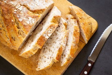 A loaf of craft bread is sliced on a cutting board with a knife