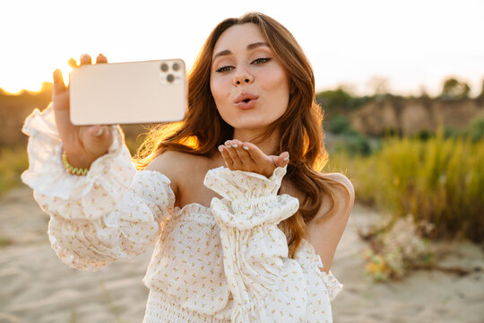 Young woman smiling and taking selfie phoro on cellphone outdoors