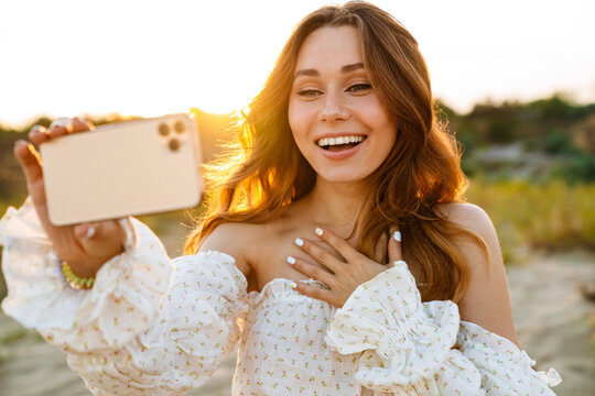 Young woman smiling and taking selfie phoro on cellphone outdoors