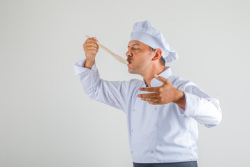Male chef trying meal in uniform, apron and hat and looking confident. front view.
