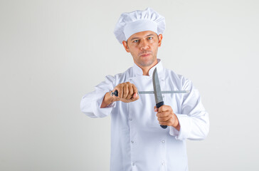 Male chef cook holding kitchen knives in uniform and hat and looking confident , front view.