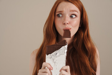 Ginger half-naked scared girl eating chocolate and looking aside