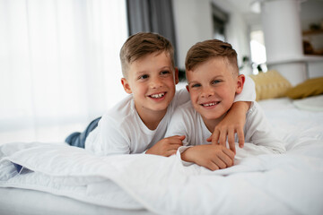 Fototapeta premium Two little brothers are playing games on the phone. Beautiful boys enjoying at home.