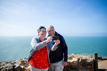 Smiling couple taking selfie, sea on background
