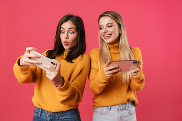 Two happy pretty girls using mobile phones isolated