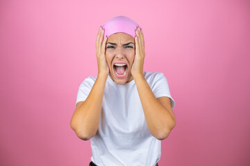 Young beautiful woman wearing pink headscarf over isolated pink background crazy and scared with hands on head, afraid and surprised of shock