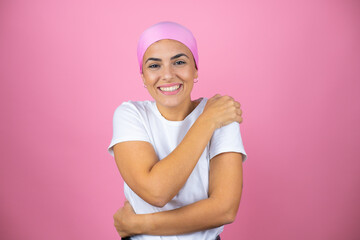 Young beautiful woman wearing pink headscarf over isolated pink background hugging oneself happy and positive, smiling confident