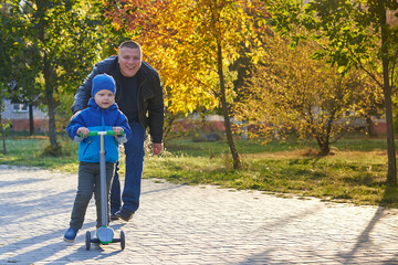 Obraz premium Dad teaches his two-year-old son to ride a scooter.