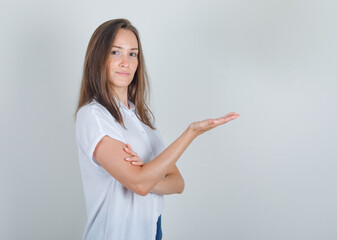 Young woman keeping open palm in white t-shirt, jeans and looking cheerful , front view.