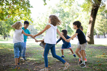 Group of children holding hands and dancing around, enjoying outdoor activities and having fun in...