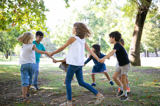 Group of children holding hands and dancing around, enjoying outdoor activities and having fun in park. Kids party or friendship concept