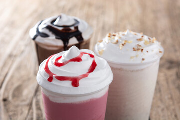 Strawberry, chocolate and white iced milkshakes on wooden table	