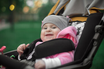 A girl in pink clothes is sitting in a yellow stroller in a Park among green trees.