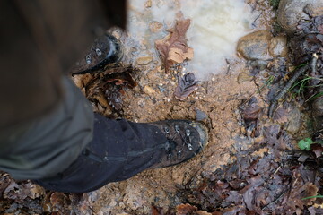 Hunter walks in the hunting area with his brown rubber boots in the muddy lane of a wood harvesters.