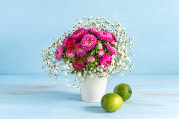 Bouquet of chrysanthemums and lime fruits on blue wooden background.