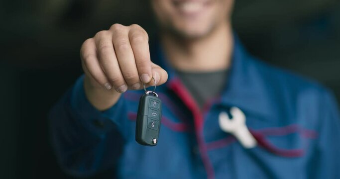 Cheerful unrecognizable auto mechanic giving car keys to camera after finishing vehicle maintenance
