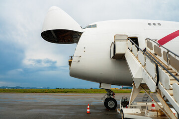 A Jumbo Jet freighter aircraft with a wide open nose cargo door waiting at a cargo ramp for a high-loader to be offloaded