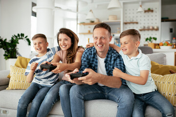 Husband and wife playing video games with joysticks in living room. Loving couple are playing video games with kids at home..