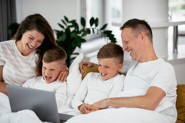 Beautiful parents with kids enjoying at home. Young family watching movie on lap top.